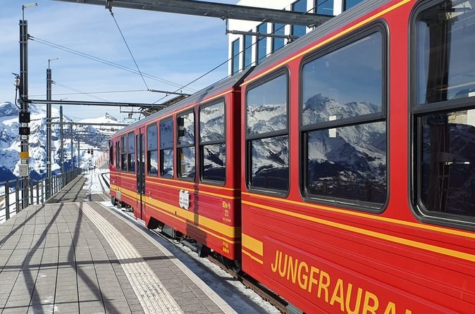 A red mountain train standing at a high station platform under a blue sky