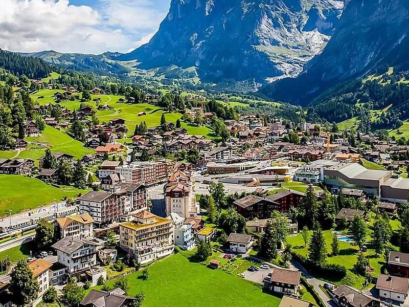 A mountain village of hotels and chalets seen from above, a rock peak behind