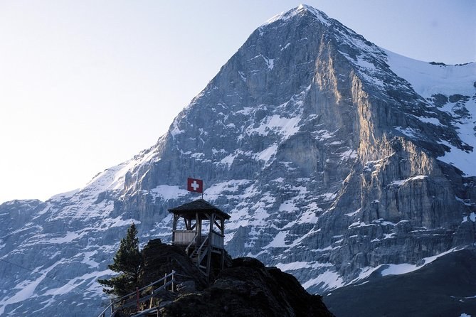 A vast limestone north face rising above a small wooden lookout with a Swiss flag