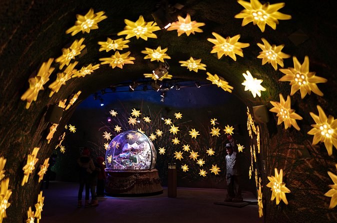 A rock tunnel hung with glowing star lanterns around a lit glass globe