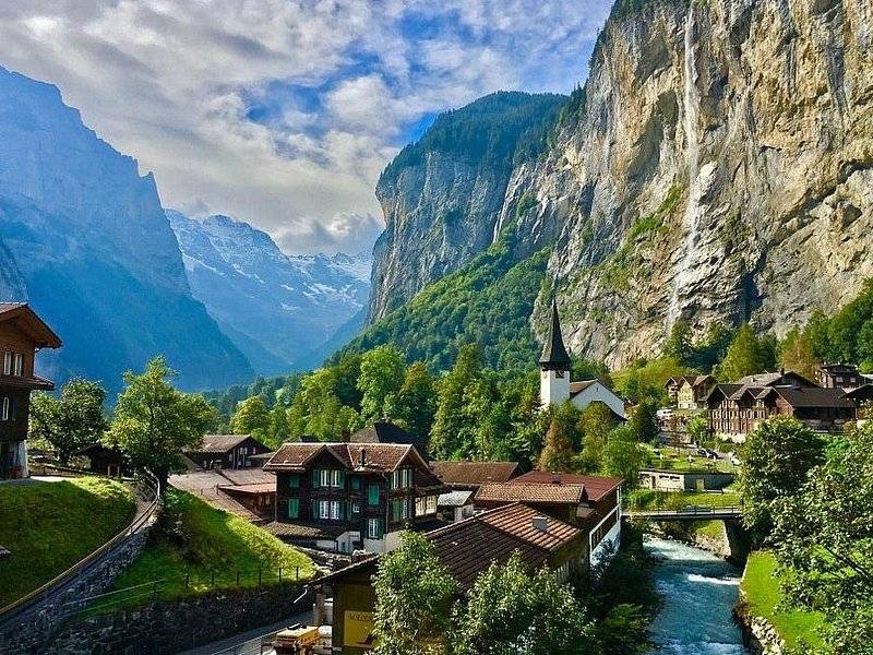 Chalets, a white church spire and a river under the limestone walls of a deep valley